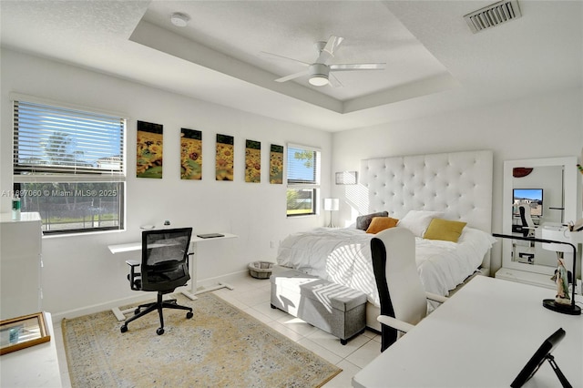 bedroom with light tile patterned flooring, visible vents, baseboards, and a tray ceiling