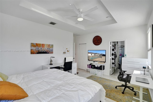 bedroom with a spacious closet, visible vents, a tray ceiling, light tile patterned floors, and a ceiling fan