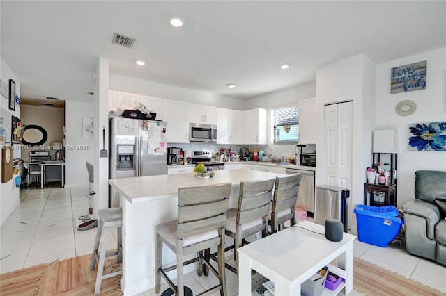 kitchen featuring stainless steel appliances, visible vents, white cabinetry, a kitchen island, and light countertops