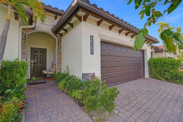 exterior space with an attached garage, stone siding, stucco siding, and decorative driveway