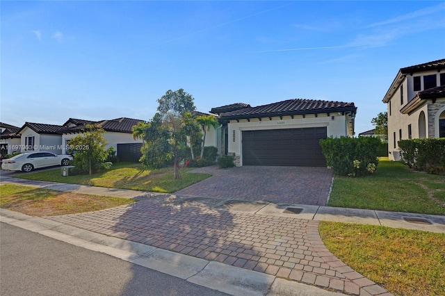 mediterranean / spanish house featuring a front lawn, a tiled roof, stucco siding, decorative driveway, and an attached garage