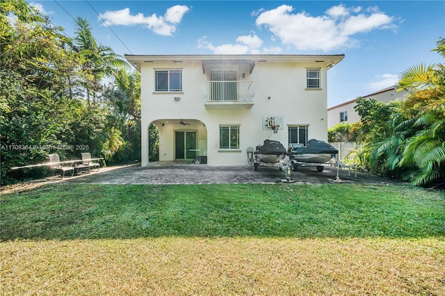 rear view of house with a balcony, ceiling fan, a patio area, and a lawn