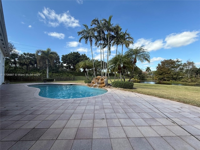 view of swimming pool featuring a patio, a water view, pool water feature, and a lawn