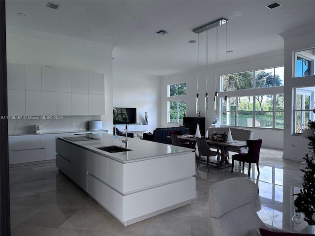 kitchen featuring sink, hanging light fixtures, a kitchen island with sink, white cabinets, and ornamental molding