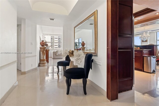 hallway featuring light tile patterned floors, a tray ceiling, and a notable chandelier