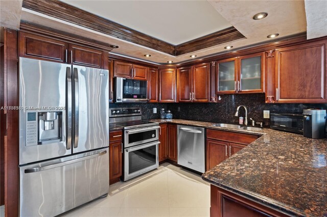 kitchen featuring backsplash, dark stone counters, stainless steel appliances, a tray ceiling, and sink