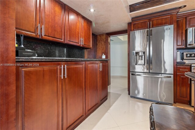 kitchen with decorative backsplash, dark stone countertops, light tile patterned floors, and appliances with stainless steel finishes