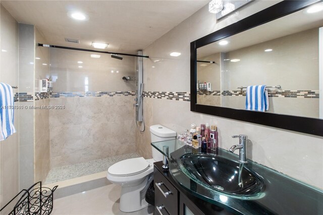 bathroom featuring toilet, vanity, tile walls, and tiled shower