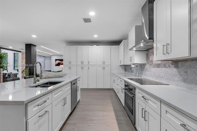 kitchen with stainless steel appliances, a sink, light countertops, backsplash, and wall chimney exhaust hood