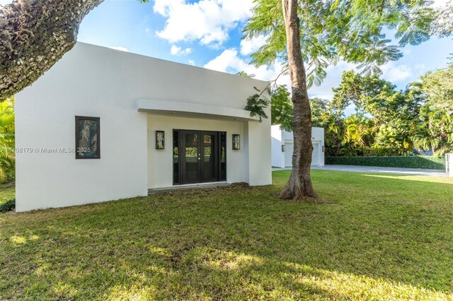 property entrance featuring french doors, a lawn, driveway, and stucco siding