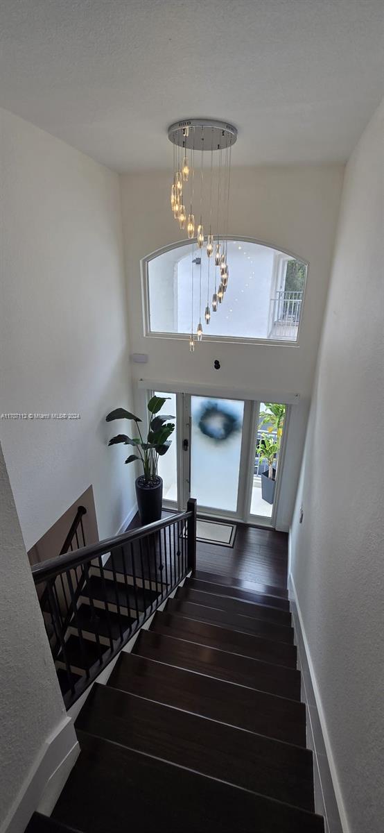 stairway featuring wood-type flooring, a high ceiling, and a notable chandelier