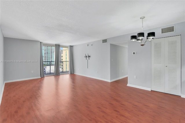 empty room with floor to ceiling windows, hardwood / wood-style floors, a chandelier, and a textured ceiling