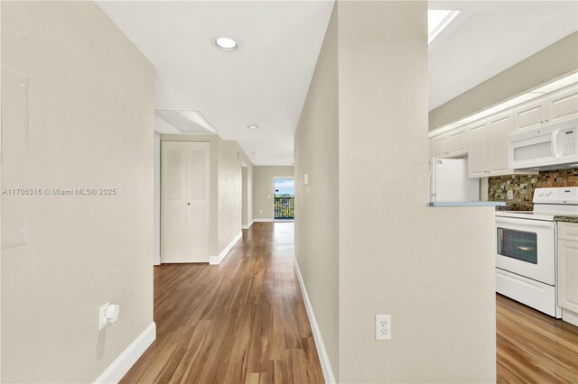 kitchen with backsplash, light stone counters, white appliances, hardwood / wood-style flooring, and white cabinetry