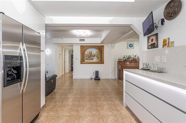 kitchen with decorative backsplash, stainless steel fridge, white cabinetry, and light tile patterned floors