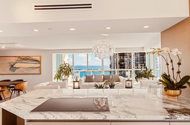 kitchen featuring black electric stovetop, light stone counters, a water view, visible vents, and open floor plan