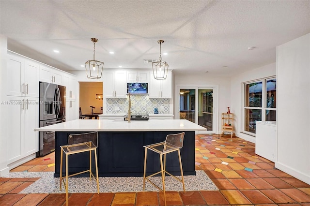 kitchen with white cabinets, decorative light fixtures, stainless steel appliances, and a kitchen island with sink