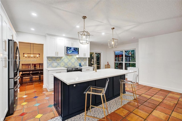 kitchen with pendant lighting, backsplash, a center island with sink, white cabinets, and appliances with stainless steel finishes