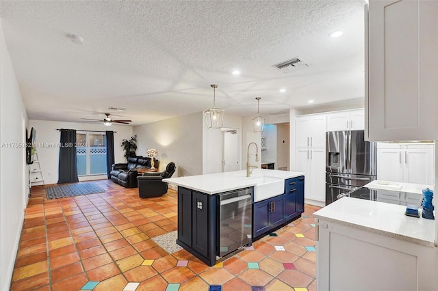 kitchen featuring stainless steel refrigerator with ice dispenser, sink, a center island with sink, decorative light fixtures, and white cabinets