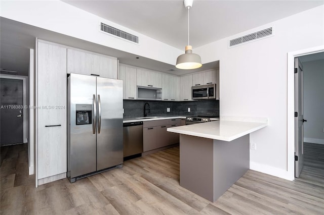 kitchen featuring sink, light hardwood / wood-style flooring, appliances with stainless steel finishes, tasteful backsplash, and decorative light fixtures