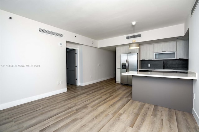 kitchen with gray cabinetry, stainless steel refrigerator with ice dispenser, hanging light fixtures, light hardwood / wood-style flooring, and kitchen peninsula