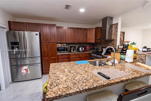 kitchen with kitchen peninsula, light stone counters, stainless steel appliances, and wall chimney range hood