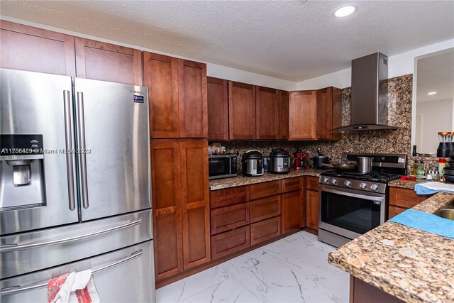 kitchen featuring light stone countertops, tasteful backsplash, wall chimney exhaust hood, a textured ceiling, and stainless steel appliances