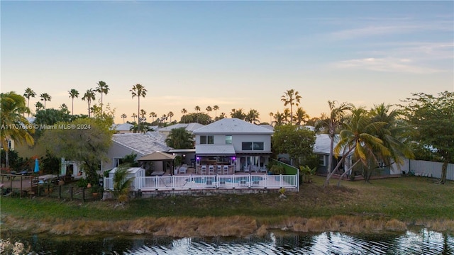 back house at dusk featuring a water view and a fenced in pool