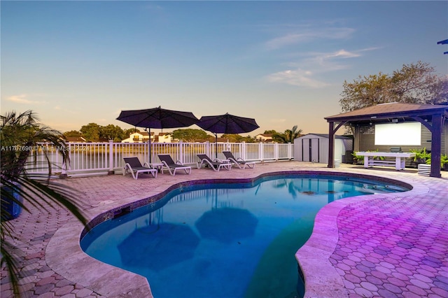 pool at dusk featuring a patio area and a storage unit