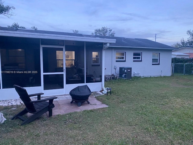 rear view of house with a fire pit, a yard, a patio, central AC unit, and a sunroom