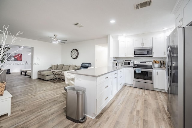 kitchen with light wood-type flooring, appliances with stainless steel finishes, kitchen peninsula, white cabinets, and backsplash