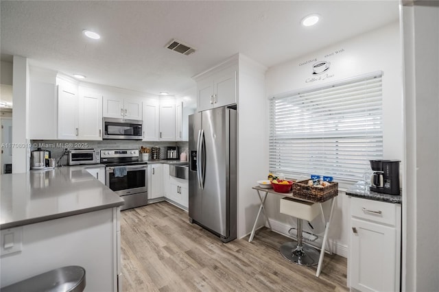 kitchen featuring white cabinetry, light wood-type flooring, tasteful backsplash, and appliances with stainless steel finishes