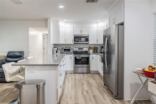 kitchen featuring appliances with stainless steel finishes, a breakfast bar area, white cabinets, backsplash, and light hardwood / wood-style floors