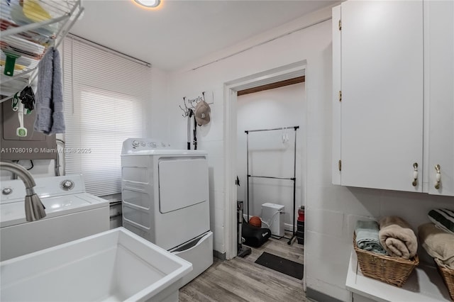 clothes washing area with washer and clothes dryer, light hardwood / wood-style floors, and cabinets