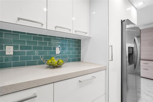 kitchen featuring tasteful backsplash, light stone countertops, stainless steel fridge, and white cabinetry