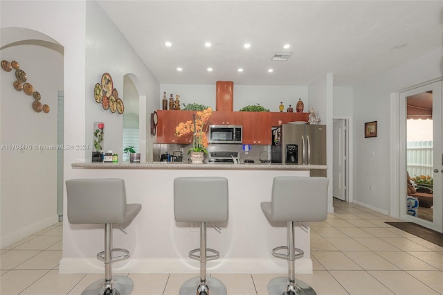 kitchen with decorative backsplash, light tile patterned floors, appliances with stainless steel finishes, kitchen peninsula, and a breakfast bar area