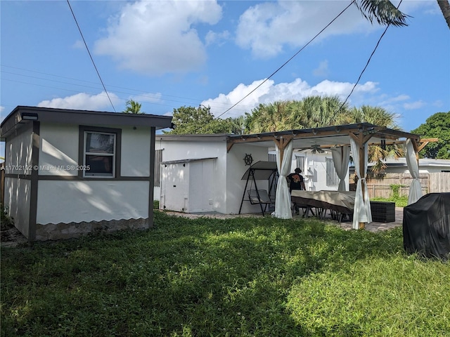 rear view of house featuring fence, a yard, and stucco siding