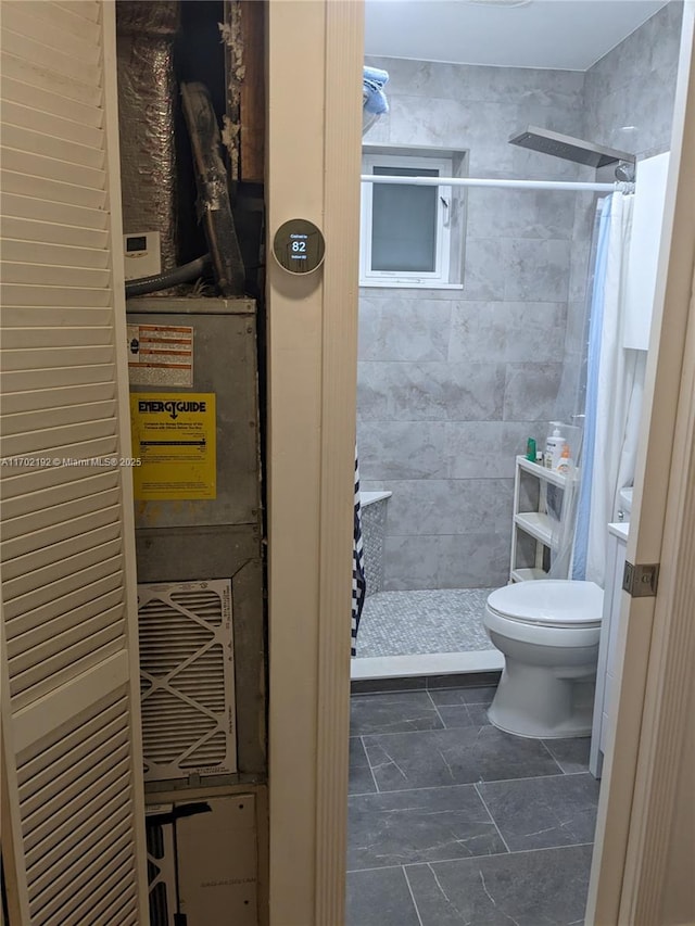 bathroom featuring toilet, stone finish flooring, and a stall shower