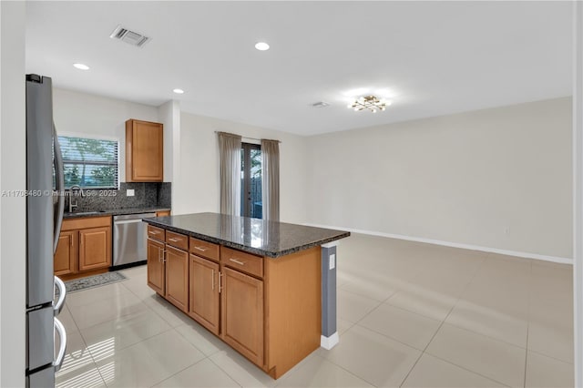 kitchen featuring stainless steel appliances, a sink, visible vents, backsplash, and a center island