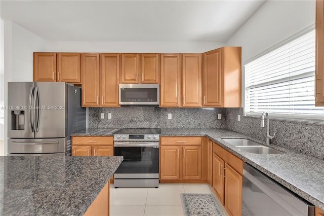 kitchen featuring light tile patterned floors, dark stone countertops, a sink, stainless steel appliances, and backsplash