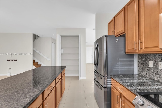 kitchen with light tile patterned floors, tasteful backsplash, dark stone counters, range, and freestanding refrigerator