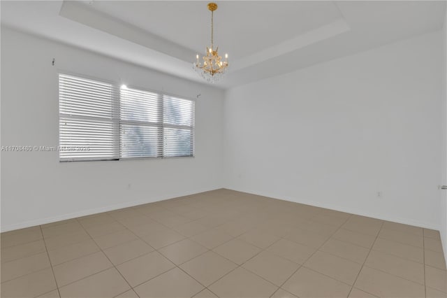 spare room with an inviting chandelier, baseboards, and a tray ceiling