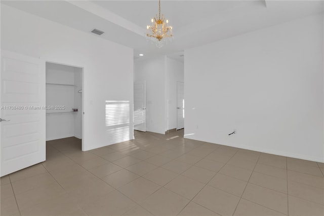 unfurnished bedroom featuring an inviting chandelier, tile patterned flooring, visible vents, and a walk in closet