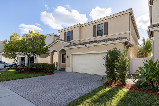 mediterranean / spanish-style home featuring decorative driveway, fence, a tiled roof, and stucco siding