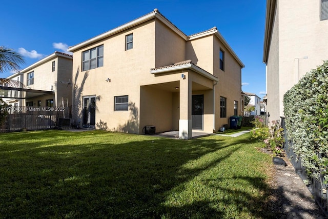 rear view of house with a patio, a lawn, fence, and stucco siding