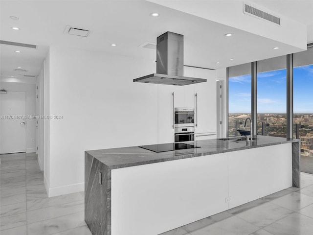 kitchen featuring dark stone counters, stainless steel double oven, black electric cooktop, island range hood, and sink