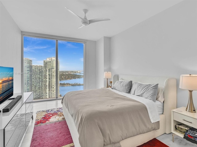 bedroom with multiple windows, ceiling fan, a water view, and a wall of windows