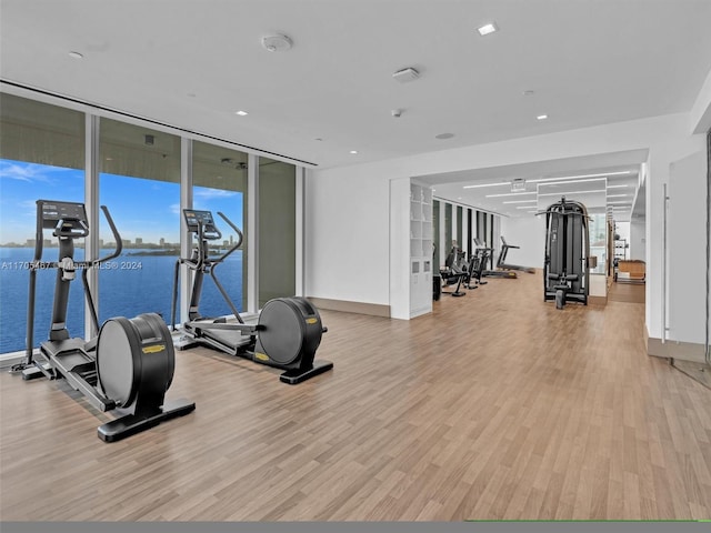 gym featuring floor to ceiling windows, light hardwood / wood-style flooring, and a water view