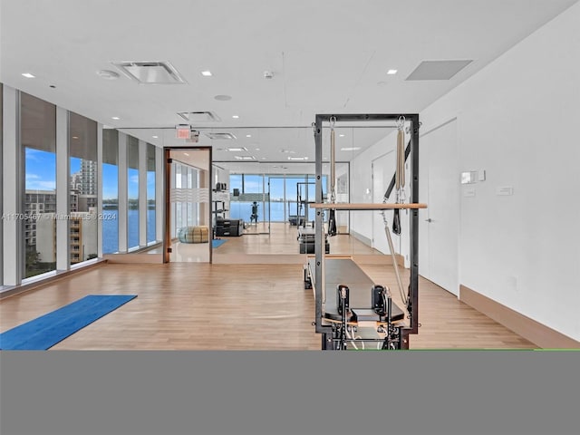 workout room with light hardwood / wood-style floors, a water view, and a wall of windows