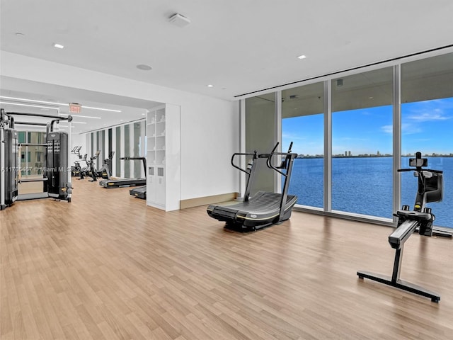 exercise room with a water view, a wall of windows, and light hardwood / wood-style flooring