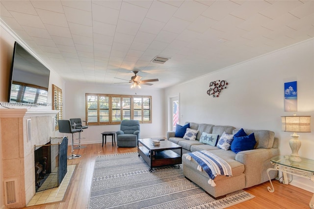 living room featuring a fireplace, hardwood / wood-style floors, ceiling fan, and ornamental molding